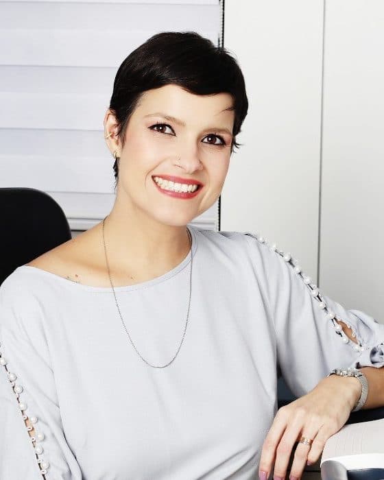 Dra. Michelle Sanches sorrindo, sentada no consultório
